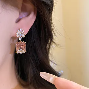 Close-up of vintage square pink crystal drop earrings with zircon accents worn on ear.