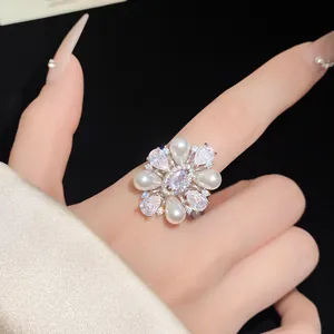 Gros plan d'une bague fleur plaquée or 14 carats avec perles et zircons sur un doigt.