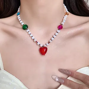 Close-up of colorful freshwater pearl necklace with red heart pendant on model's neck.