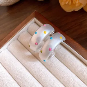 Belles boucles d'oreilles créoles argentées avec motif à pois colorés dans une boîte