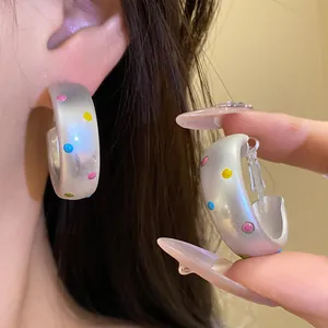 Gros plan de créoles argentées avec des pois colorés portées sur l'oreille et la main.