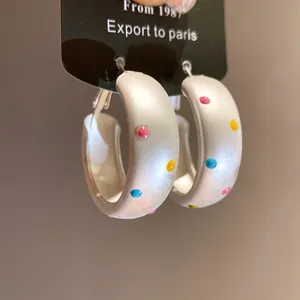Gros plan détaillé de boucles d'oreilles créoles blanches mates à pois colorés