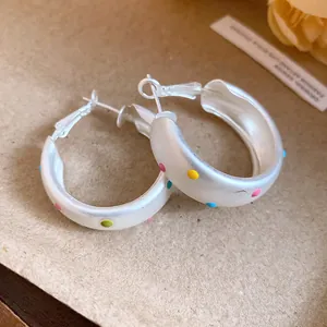 Détail en gros plan de boucles d'oreilles créoles argentées mates aux pois émaillés colorés
