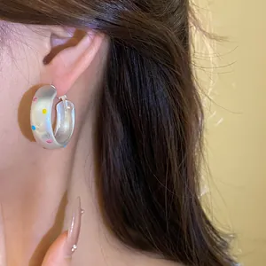 Gros plan d'une boucle d'oreille créole en argent avec des points colorés sur l'oreille