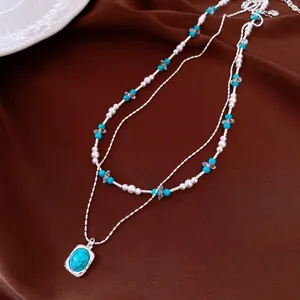 Close-up of double-layered necklace with turquoise beads and oval pendant on brown fabric
