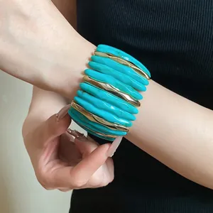 Wide marbled turquoise acrylic cuff bracelet with gold spacers on woman's wrist.