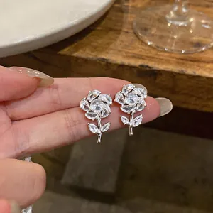 Dettaglio degli orecchini a rosa in zircone tenuti in mano, squisita fattura.