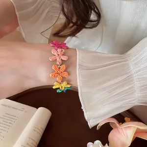 Bracciale a fiori in rafia colorata indossato al polso per uno stile estivo vivace.
