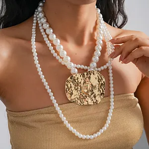 Close-up of layered pearl necklace with chunky gold crumpled metal pendant.