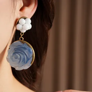 Primo piano di orecchini vintage con rosa in resina blu e perle bianche su modella