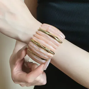 Detailed view of fashionable marbled pink acrylic bracelet with gold accents on wrist