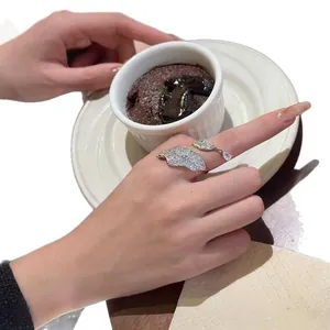 Detailed view of a zircon leaf-shaped open ring on a finger in a café setting.