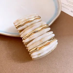 Close-up detail of marble-effect acrylic and gold wavy metal spliced stretch bracelet
