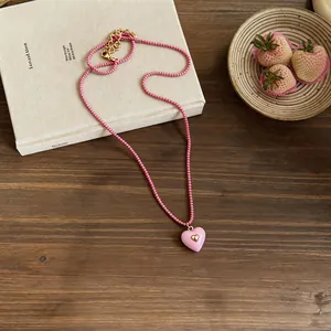 Close-up of pink beaded necklace with a heart resin pendant on a rustic wooden desk.