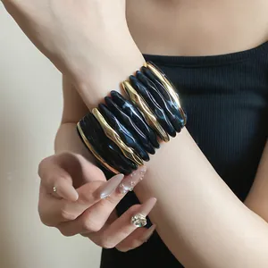 Macro detail shot of a chunky acrylic marbled and gold metal wavy bangle bracelet on wrist