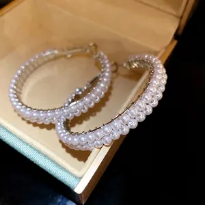 Elegant white pearl hoop earrings with silver needles displayed in a jewelry box.