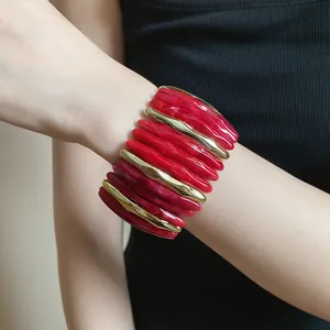 Detail of red marbled acrylic and gold-tone metal stretch bracelet worn on wrist