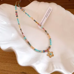 Handmade colorful bohemian beaded necklace featuring a gold flower pendant on a white shell dish