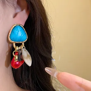 Primer plano de pendientes vintage triangulares con piedra azul y perlas.