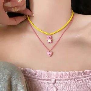 Close-up of layered necklaces with yellow beads, pink resin bear and heart pendants.