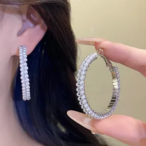 Detail shot of elegant large pearl-encrusted hoop earrings with silver needles.