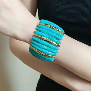 A detail shot of a chunky turquoise acrylic bangle with elegant gold accents on a wrist.