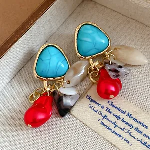 Detalle de pendientes vintage de triángulo turquesa con perla roja y borlas en bandeja de joyas