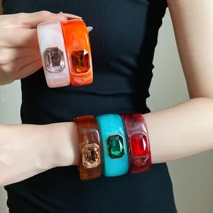 Detailed view of colorful resin bangles with large emerald-cut crystals on model arm