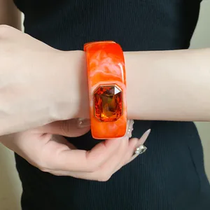 Detailed shot of an orange marbled resin square bangle with a large amber gemstone.