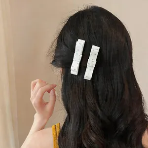 Rear view detail of two white floral fabric bow hair clips on dark wavy hair