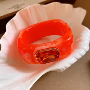 Close-up of a vibrant orange resin square bangle with a large central orange gemstone