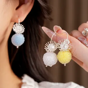 Close-up detail of textured glass sphere ear hook earrings in blue, white, and yellow
