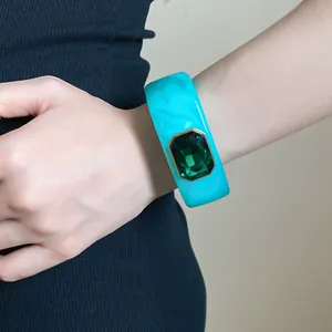 Close-up view of a wide cyan marble resin bangle with a large emerald green gemstone