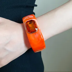 Detailed close-up of orange marbled resin bangle with a large amber gemstone on a wrist.