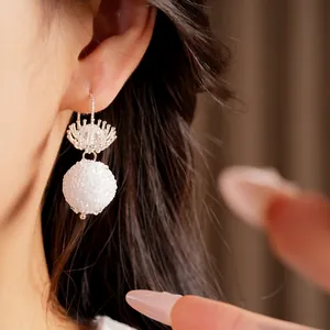 Close-up detail of minimalist silver flower hook earring with white textured bead