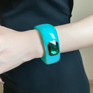 Close-up of a turquoise resin square bangle with a large emerald-cut green gemstone detail.