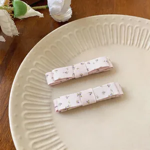Close-up of pink fabric bow hair clips with purple floral prints on a beige plate.