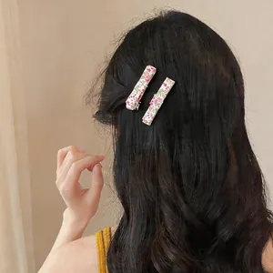 Detailed macro view of two floral print fabric duckbill hair clips styled on dark wavy hair
