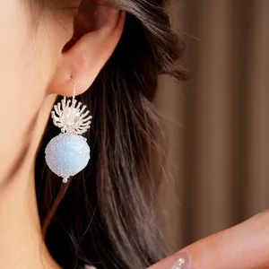 Close-up detail of a light blue textured ball earring with elegant floral silver hook.