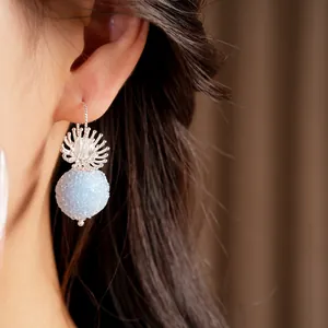 Close-up detail of a minimalist silver hook earring with a light blue frosted glass sphere