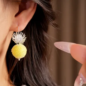 Close-up detail showing a unique yellow textured spherical drop earring with silver floral top