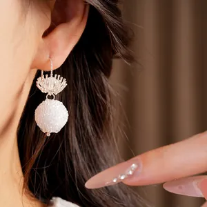 Detailed view of elegant glass flower and white textured ball earrings on a model's ear