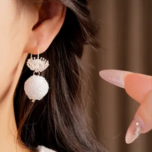 Close-up detail of white frosted round glass flower hook earrings on a model's ear