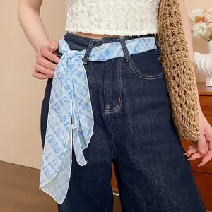 Detailed macro view showing a blue checkered silk scarf elegantly tied as a belt on denim pants