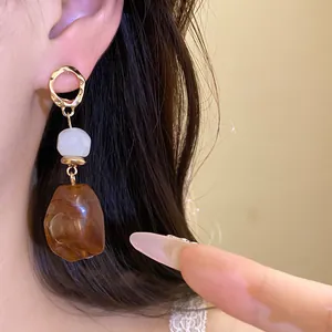 Detailansicht von Vintage-Ohrringen mit bernsteinfarbenem Harzanhänger am Ohr des Models.