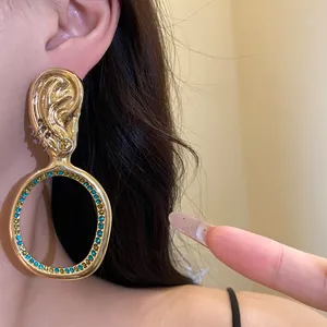 Primo piano di orecchino a cerchio dorato vintage con strass turchesi indossato all'orecchio