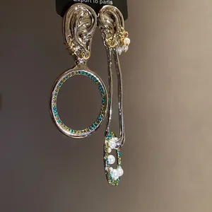 Dettaglio di orecchini d'argento asimmetrici con perni a forma di orecchio e cristalli