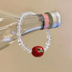 Beaded bracelet with clear faceted beads and a red resin apple pendant on a glass bottle