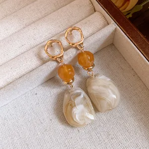 Nahaufnahme der Maillard-Retro-Resin-Ohrringe mit Marmorierung und goldenen Creolen.
