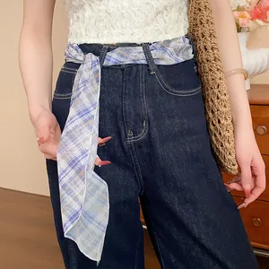 Detail of a blue plaid scarf used as a waist belt accessory on denim jeans